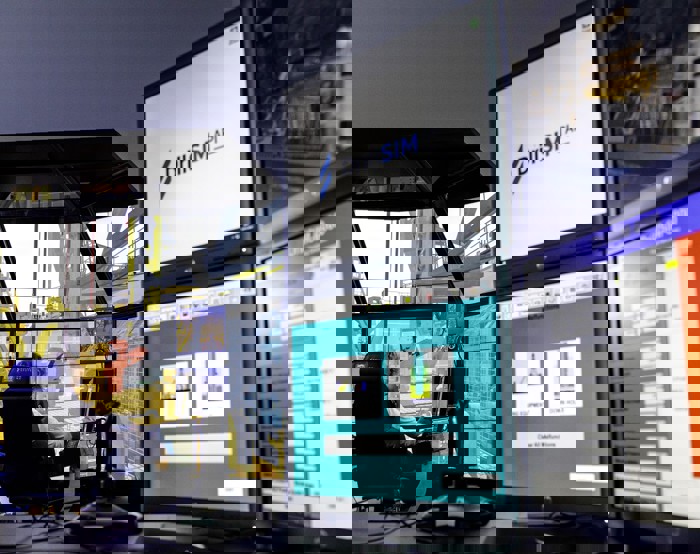 Multiple computer monitors in a control room display simulation software for drilling operations, one screen showing "DrillSIM API." A person is seated, focusing on the large central monitor.