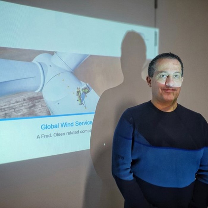 A person stands in front of a projection screen displaying "Global Wind Services" and an image of a wind turbine.