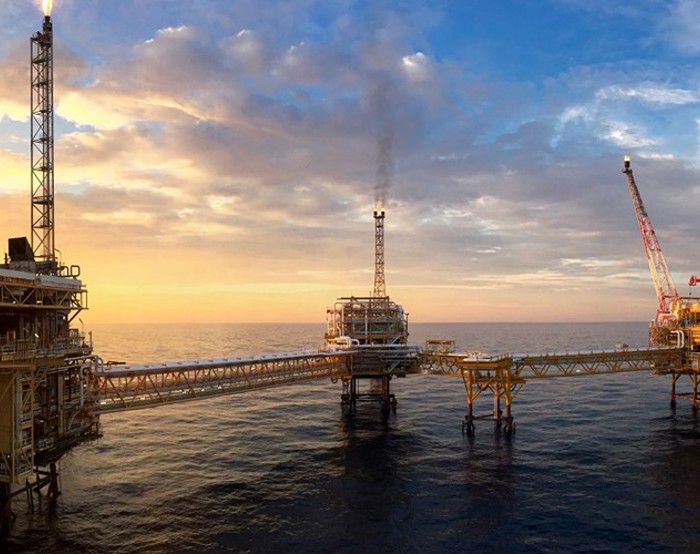 An offshore oil platform at sunset with a network of connected walkways over the ocean and a crane on the right side.