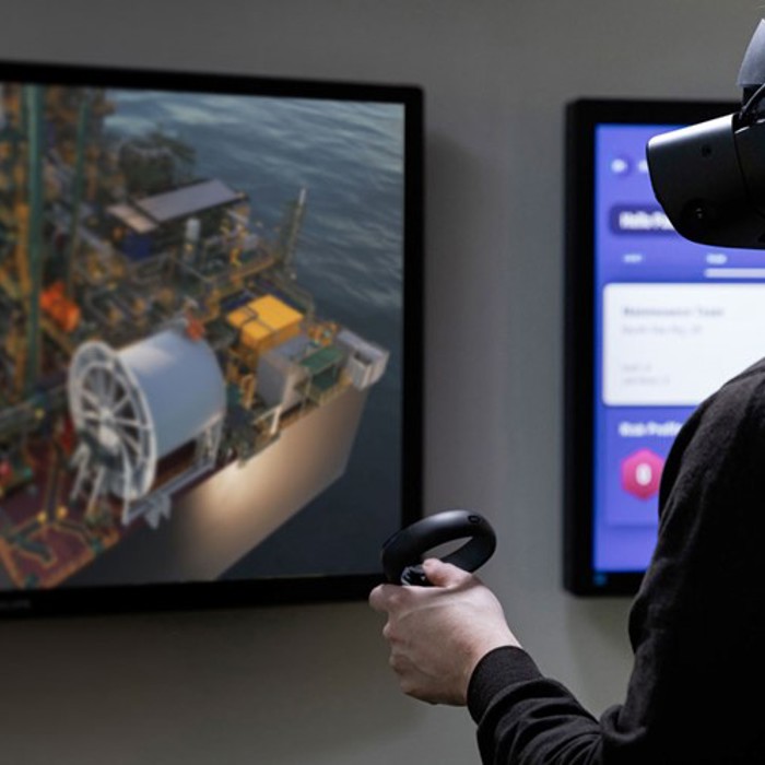 A person wearing a VR headset and holding a controller is viewing a detailed 3D model of an industrial facility displayed on a screen.