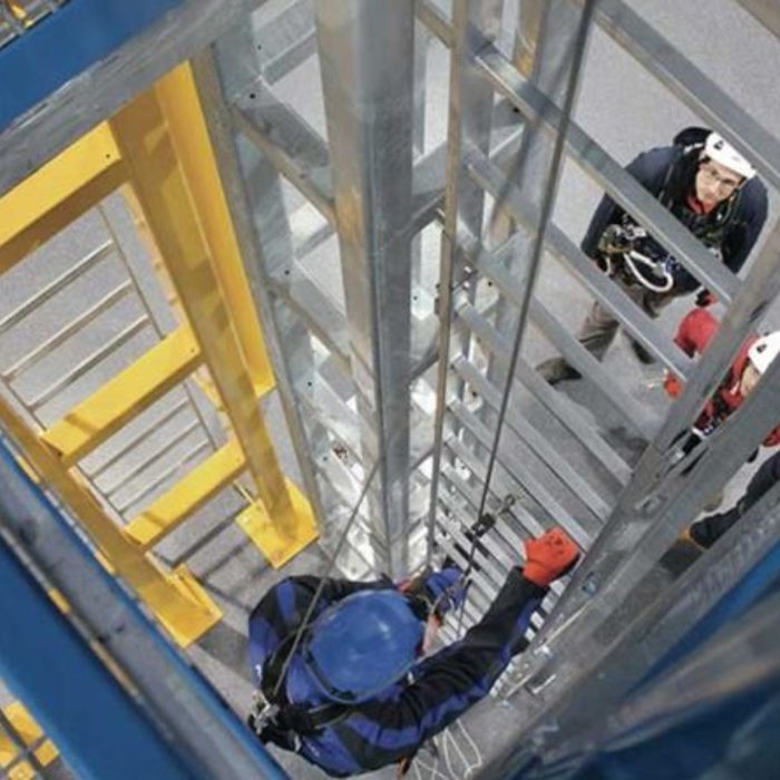 Workers wearing safety gear climb and stand on a metal industrial structure.