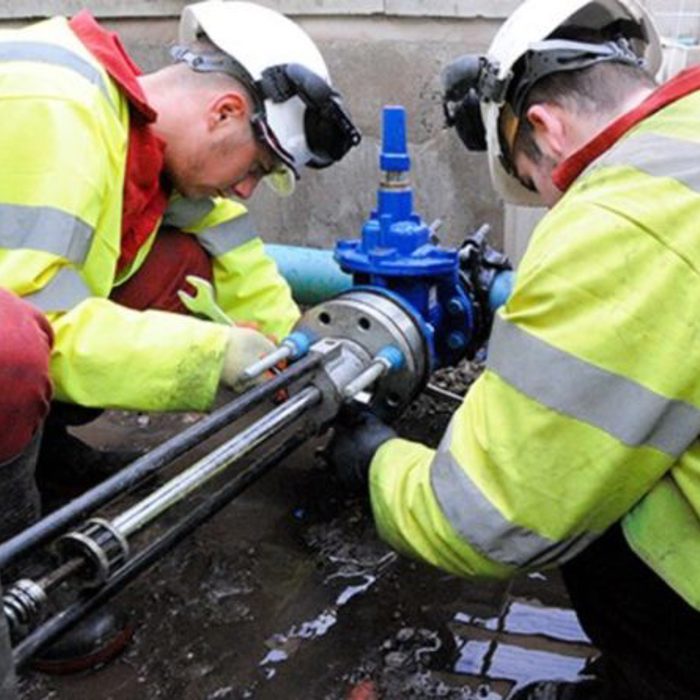 Two workers in high-visibility jackets and helmets repair a pipe on a construction site.