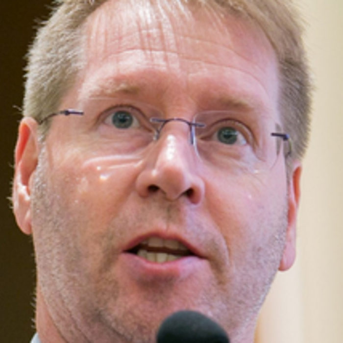 A man with glasses and a short beard speaks into a microphone.