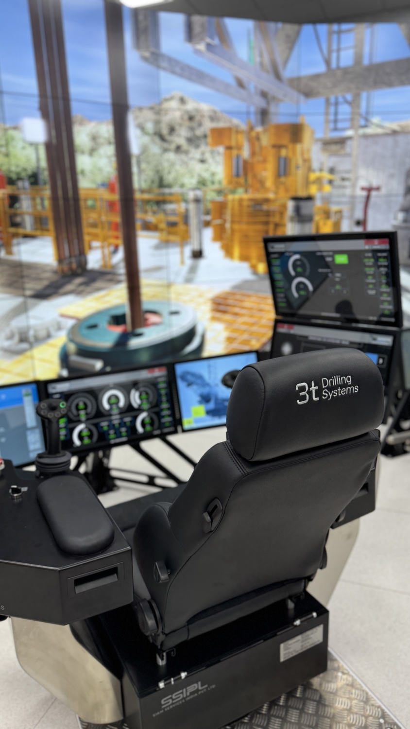 Picture from behind a training simulator showing black chair, controls and screens displaying drilling floor.