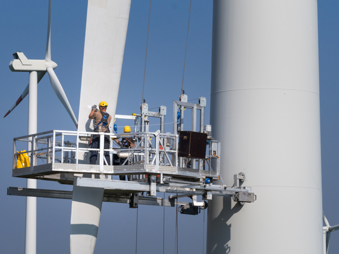 Workers on a platform engage in specialized training while performing maintenance on a large wind turbine.